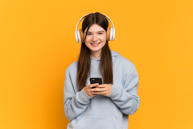 Young girl over isolated listening music with a mobile and looking front