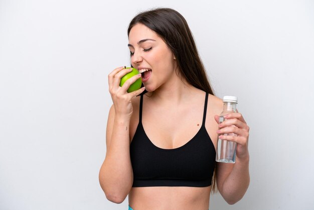 Young girl isolated on white background with a bottle of water and eating an apple