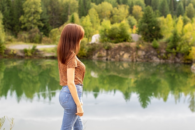 young girl in jeans walks near a beautiful lake in cloudy weather.