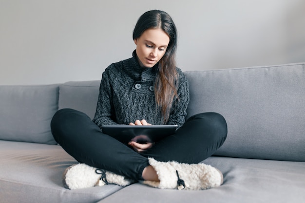 Young girl in knitted sweater at home on the sofa with digital tablet