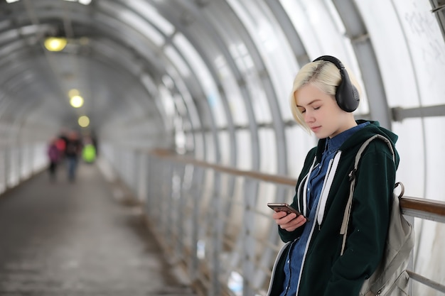 Photo young girl listens to music in big headphones in the subway tunnel