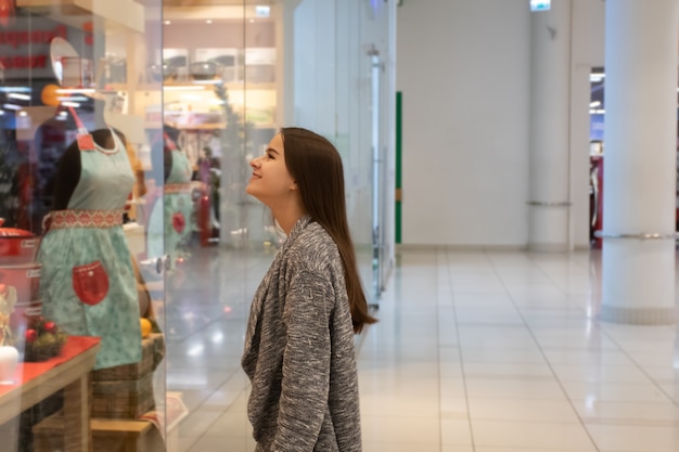 A young girl looks at shop windows, chooses gifts in a mall