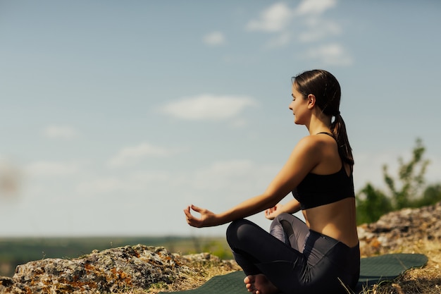 Young girl meditates in the Lotus position on top of the mountains.