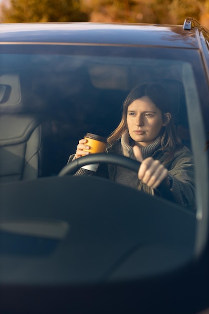 Young girl in the morning goes to work by car and drinking coffee View through the windshield