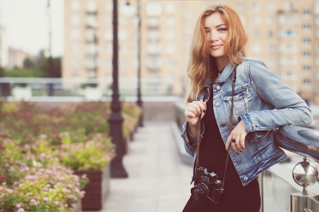 Young girl photographer walking along the street in a jeans jacket with an old camera