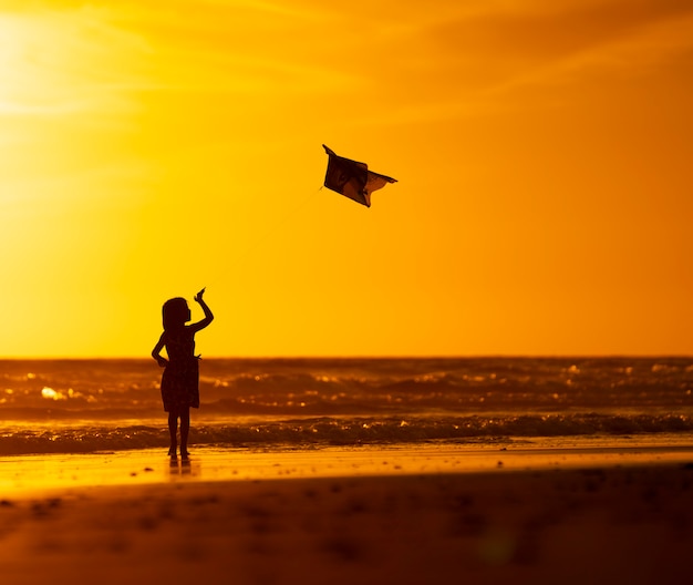 young girl playing with kite on the beach at sunset