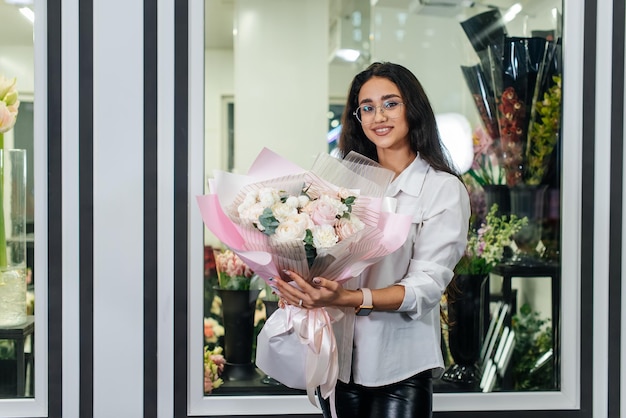 A young girl poses with a beautiful festive bouquet against the background of a cozy flower shop Floristry and bouquet making in a flower shop Small business