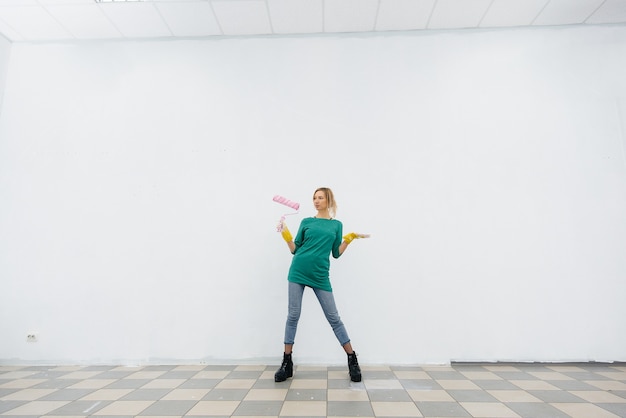 Photo a young girl poses with a roller in front of a white wall. repair of the interior.