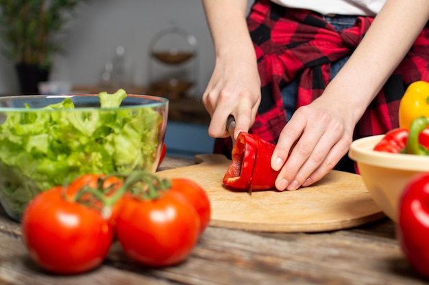 Young girl prepares a vegetarian salad in the kitchen, she chops pepper, the process of preparing healthy food, close-up