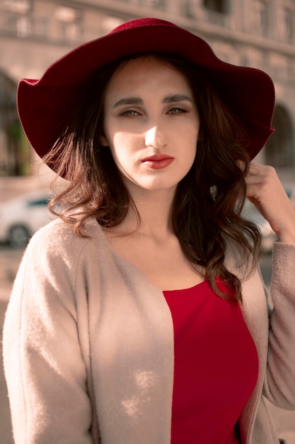 A young girl in a red dress and hat walks around the city.