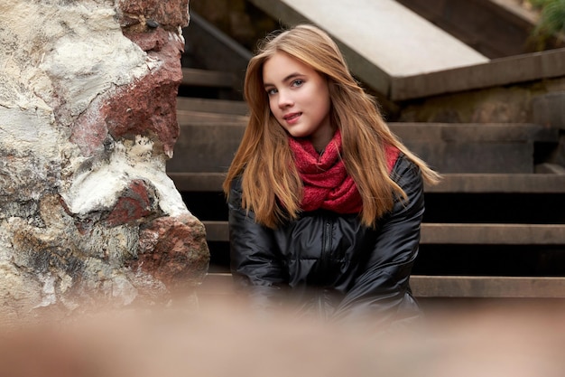 A young girl in a red skirt sits on the steps in the park in autumn