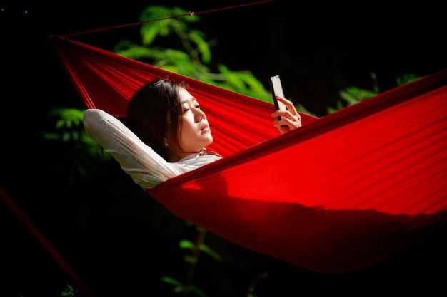 Young girl relaxing in hammock and looking to his mobile phone in the morning