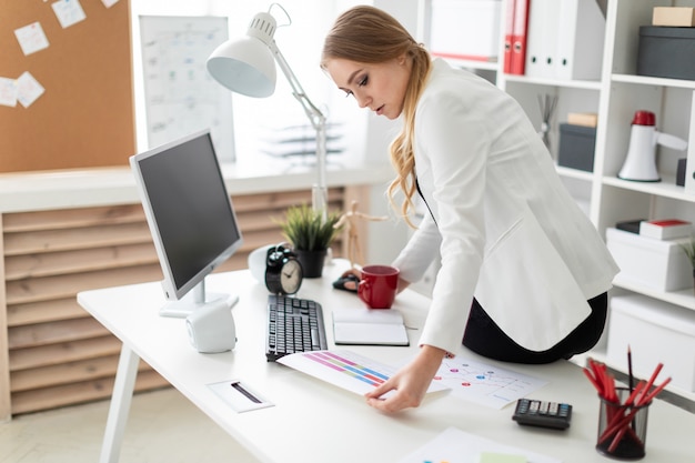 The young girl sat down on the desk in the office and worked with a computer and documents.