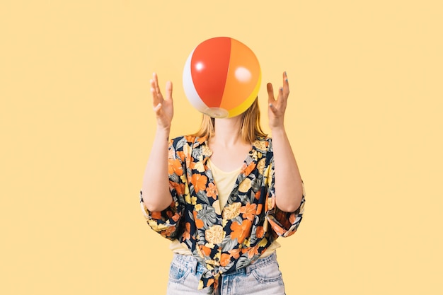 Young girl in shorts and flowered shirt throwing colorful beach ball on yellow background