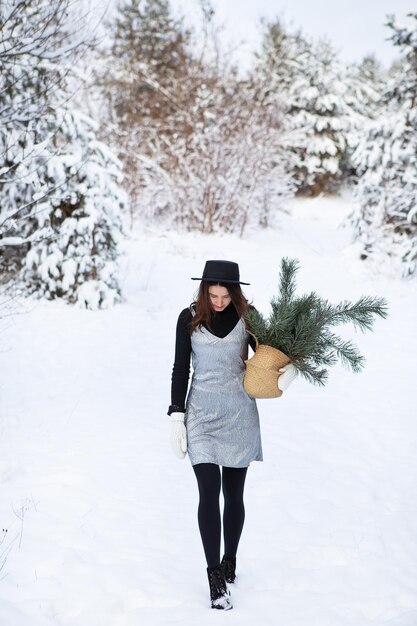 A young girl in a silvery dress and hat stands with her back in the middle of a beautiful winter forest