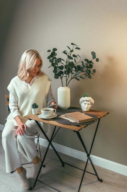 A young girl sits at a coffee table with a phone in her hands, distracted from the book. Side view.