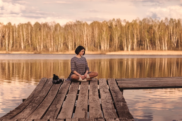 Young girl sits on a pier in a summer dress