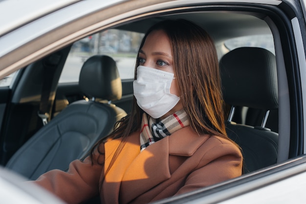 A young girl sits behind the wheel in the car in the mask during the global pandemic and coronavirus. Quarantine