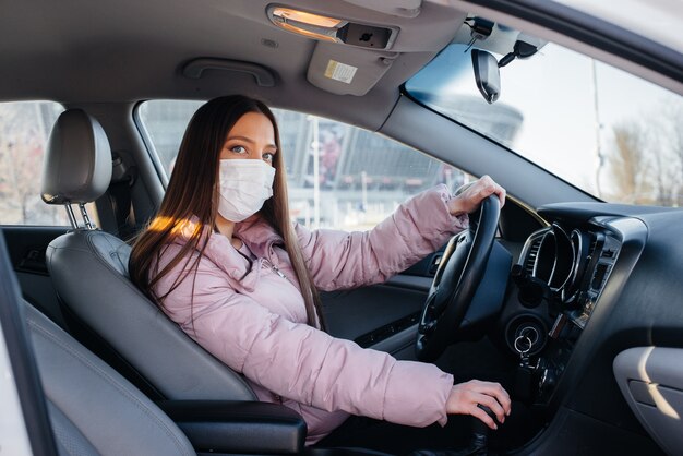 A young girl sits behind the wheel in the car in the mask during the global pandemic and coronavirus. Quarantine.