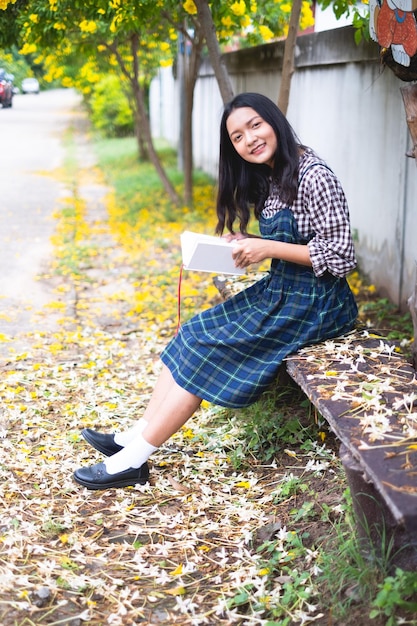 Young girl sitting on a bench reading a book under a beautiful tree