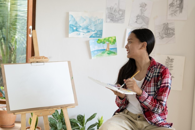 Young girl sitting on a chair with easel for drawing hold Color palette and brush in the room