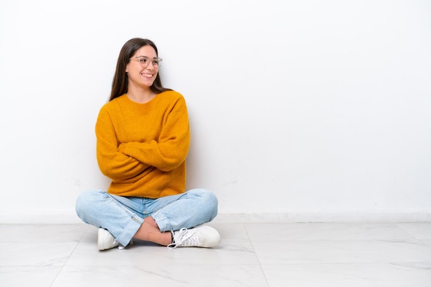 Young girl sitting on the floor isolated on white background happy and smiling