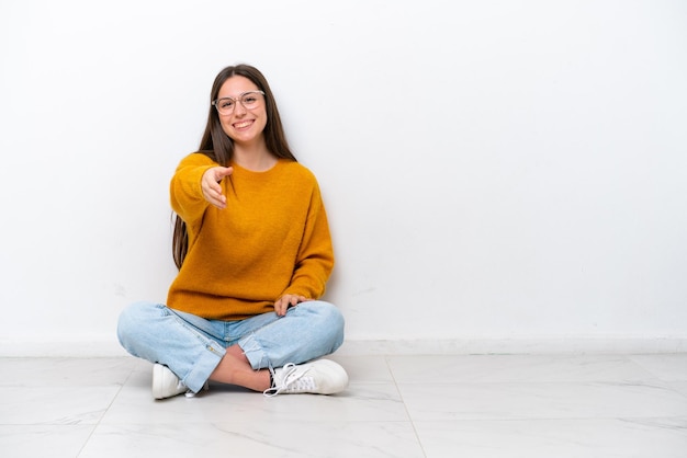 Young girl sitting on the floor isolated on white background shaking hands for closing a good deal