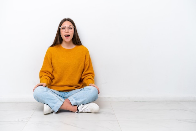 Young girl sitting on the floor isolated on white background with surprise facial expression