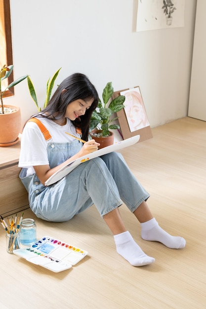 Young girl sitting on the floor and painting on paper at home Hobby and art study at home