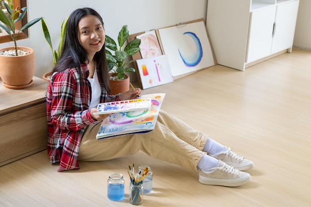 Young girl sitting on the floor and painting on paper at home Hobby and art study at home