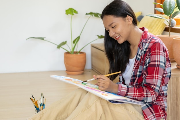 Young girl sitting on the floor and painting on paper at home Hobby and art study at home