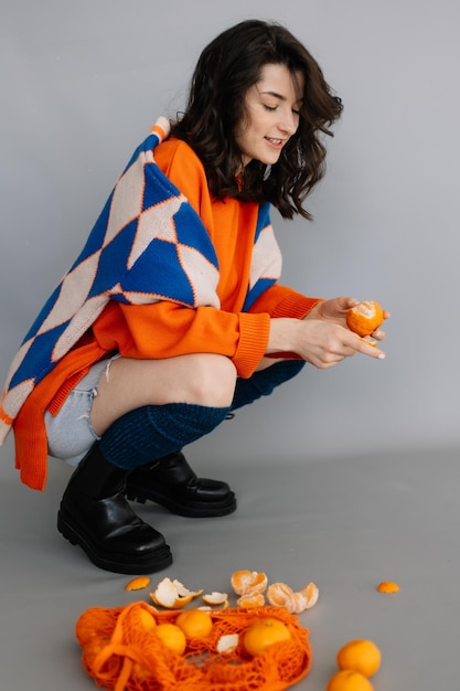 Young girl sitting on the floor in a photo studio with tangerines in her hands posing for a photo throwing tangerines into the camera laughing and having fun Bright emotions