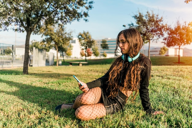 Young girl sitting on the grass in a park looking at the smartphone with headphones