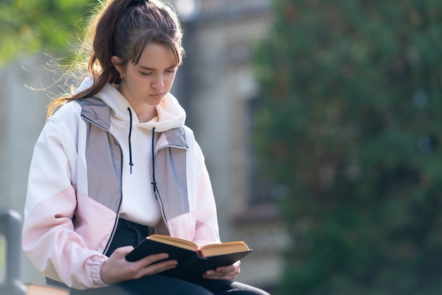 Young girl sitting quietly outdoors reading a book