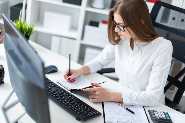 Young girl sitting at the table and working with a computer, documents and calculator