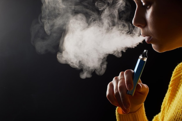 Young girl smokes a vape closeup on a dark background