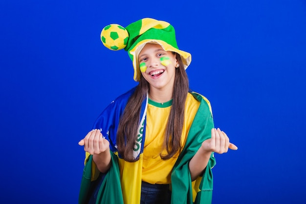 Young girl soccer fan from Brazil dressed in hat and flag calling with your hands