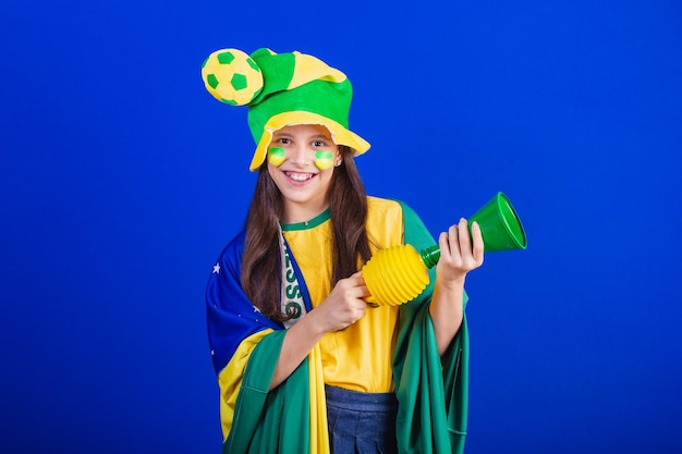 Young girl soccer fan from Brazil dressed in hat and flag making noise with horn