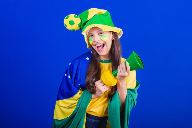 Young girl soccer fan from Brazil dressed in hat and flag making noise with horn