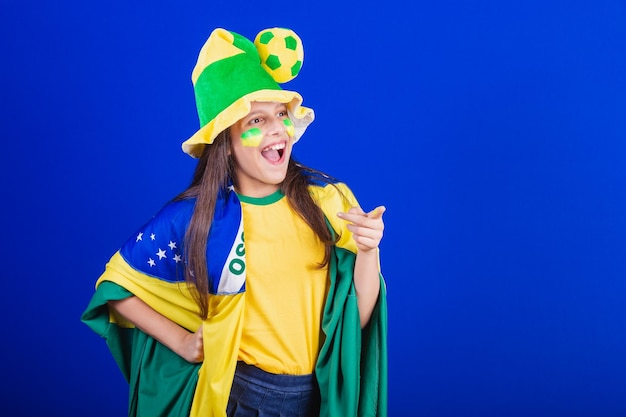 Young girl soccer fan from Brazil dressed in hat and flag pointing at something far away