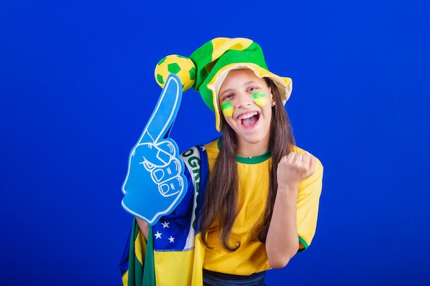 Young girl soccer fan from Brazil dressed in hat and flag using foam finger partying amazing