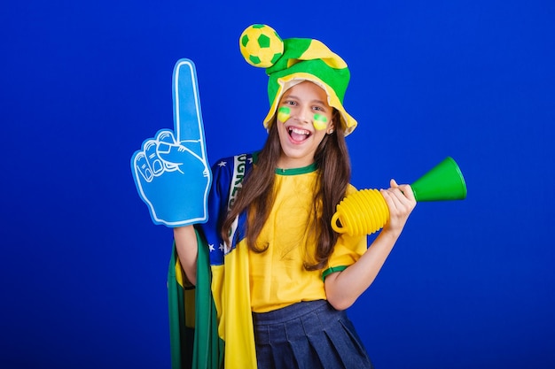 Young girl soccer fan from Brazil dressed in hat and flag using foam finger