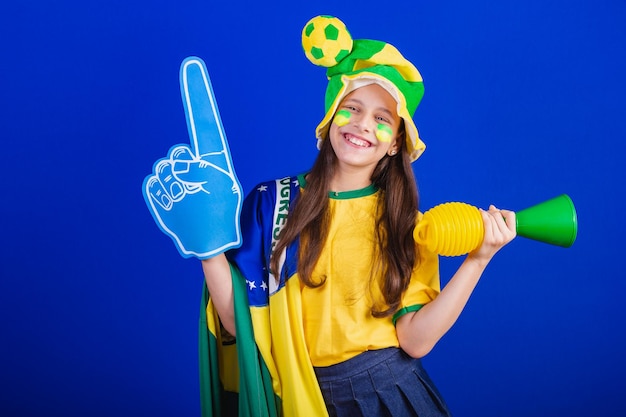 Young girl soccer fan from Brazil dressed in hat and flag using foam finger