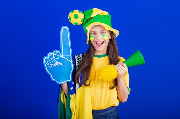 Young girl soccer fan from Brazil dressed in hat and flag using foam finger