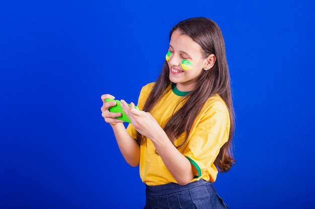 Young girl soccer fan from Brazil holding cellphone watching game cheering for Smartphone applications