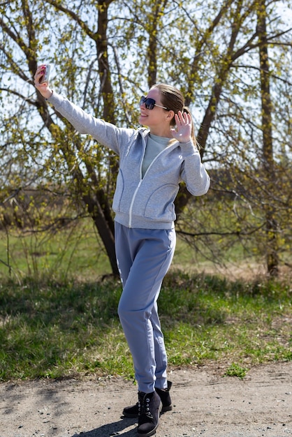 A young girl in sportswear after a run in the park is resting taking a selfie on the phone or chatting in a video chat spring time