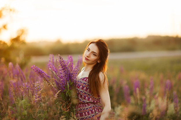 Young girl stand in field overlooking lavender field. Smiling carefree caucasian girl in dress enjoying the sunset