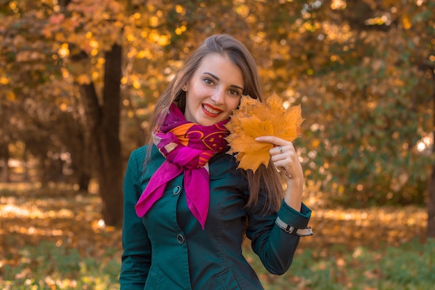 A young girl stands in autumn Park and keeps the leaves in hand