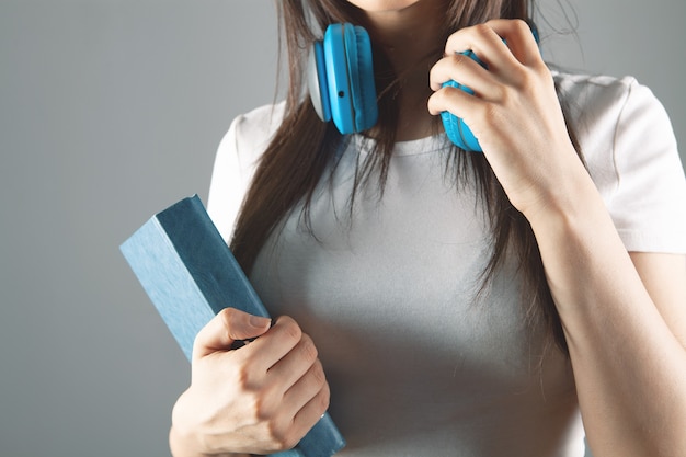 A young girl stands in headphones with a book