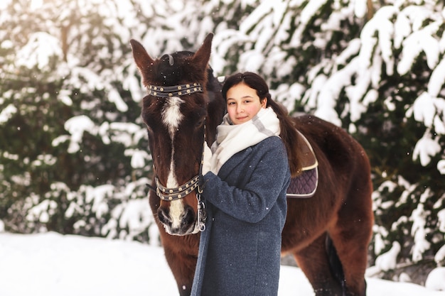 A young girl stands next to a horse in the winter outdoors